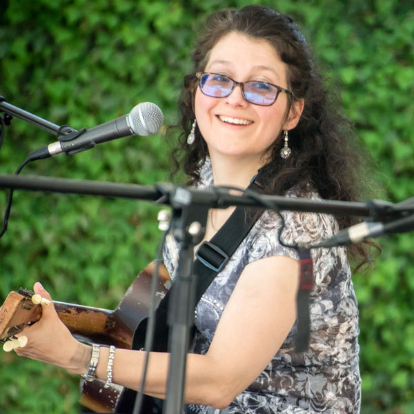 “Close-up photograph of a woman singing and playing the guitar, unfocussed background.”